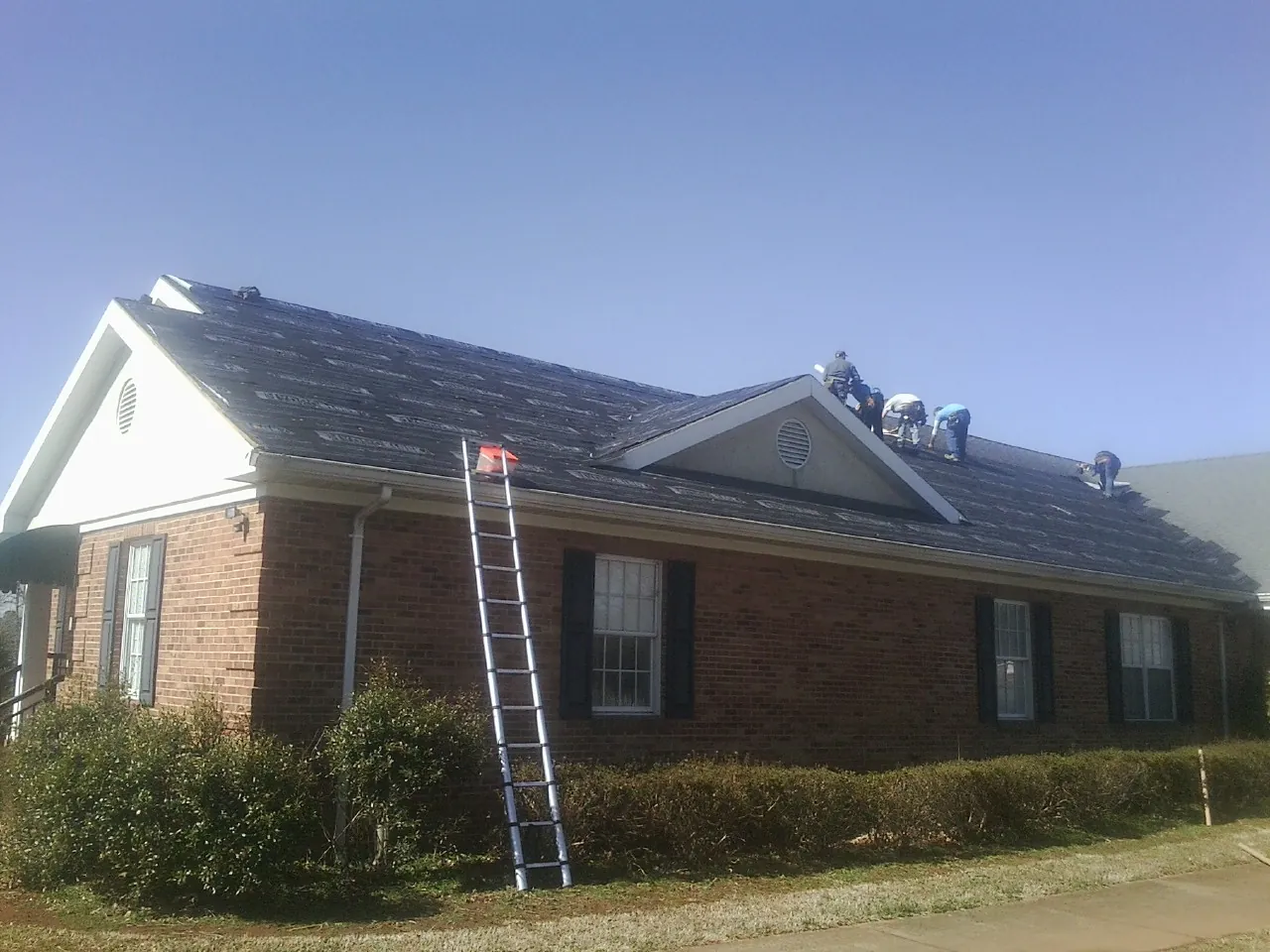 Crew tearing shingles off a brick ranch roof with a ladder set — Emergency Roof Repair work by our crew in Sweet Home