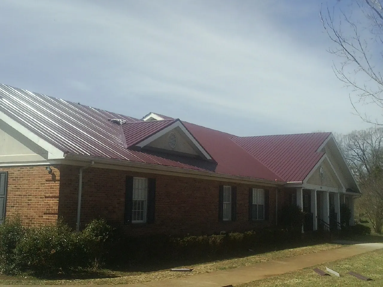 Red metal roof with gabled entries on a long brick building, from a Hail Damage Roof Repair job in Sweet Home