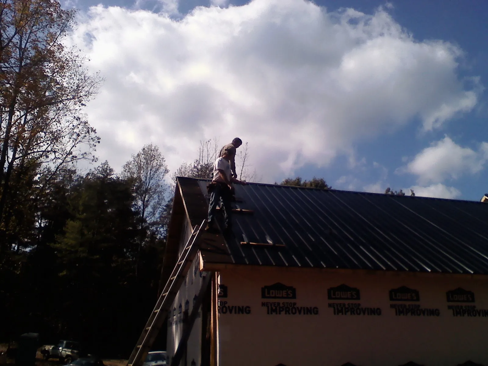 Roofer fastening dark metal panels high against a cloudy sky, from a Roof Inspection job in Sweet Home