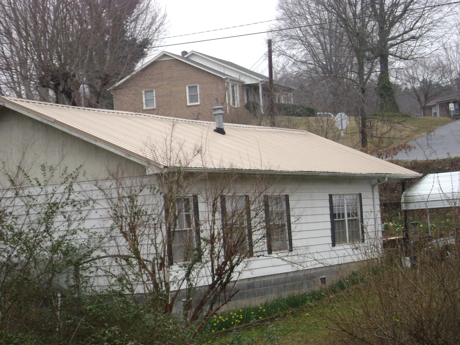 Tan metal roof on a white sided house set into a hillside — Commercial Roofing by Roofing Brothers in Sweet Home